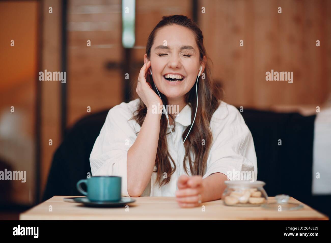 Laughing happy young woman sitting at table at home behind computer laptop and talking on video call. Girl female with portable Stock Photo