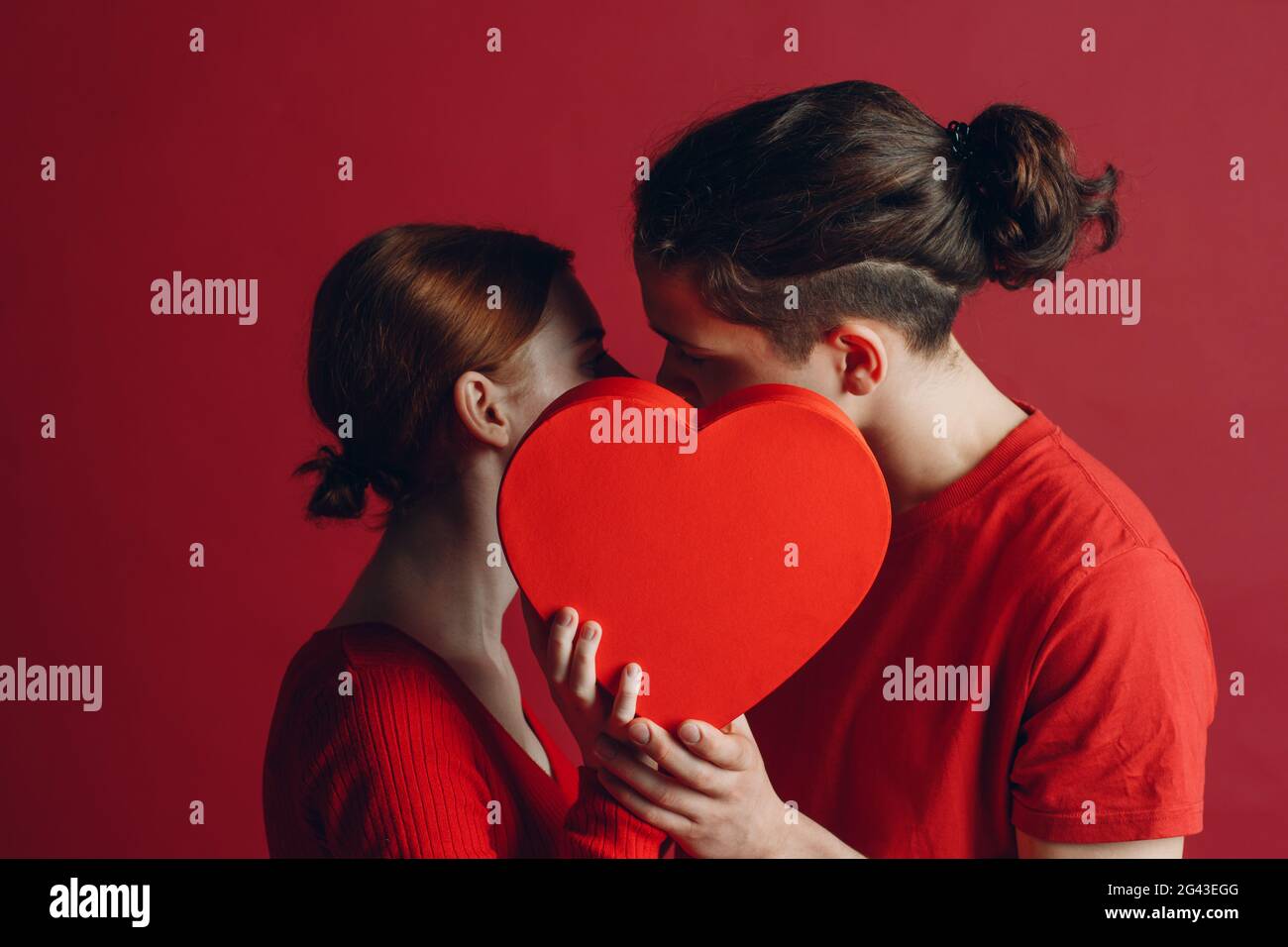 Man and woman young couple kissing and hiding behind heart-shaped box Stock Photo