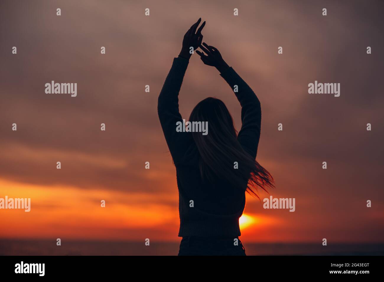 Young woman silhouette on the seashore with hands up. Stock Photo