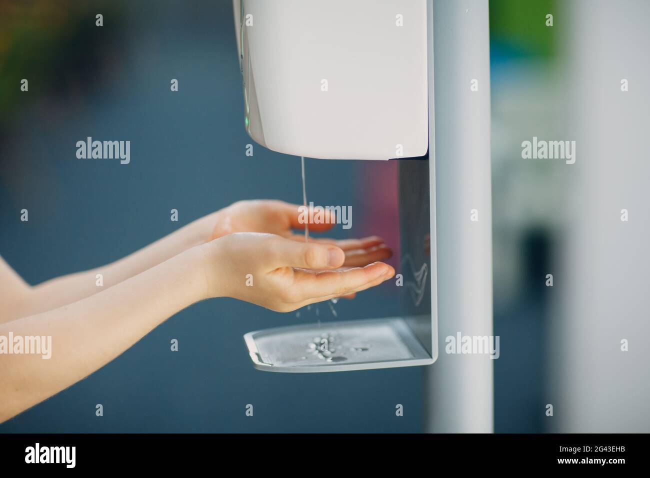 Child boy kid using automatic alcohol gel dispenser spraying on hands sanitizer machine antiseptic disinfectant, new normal life Stock Photo