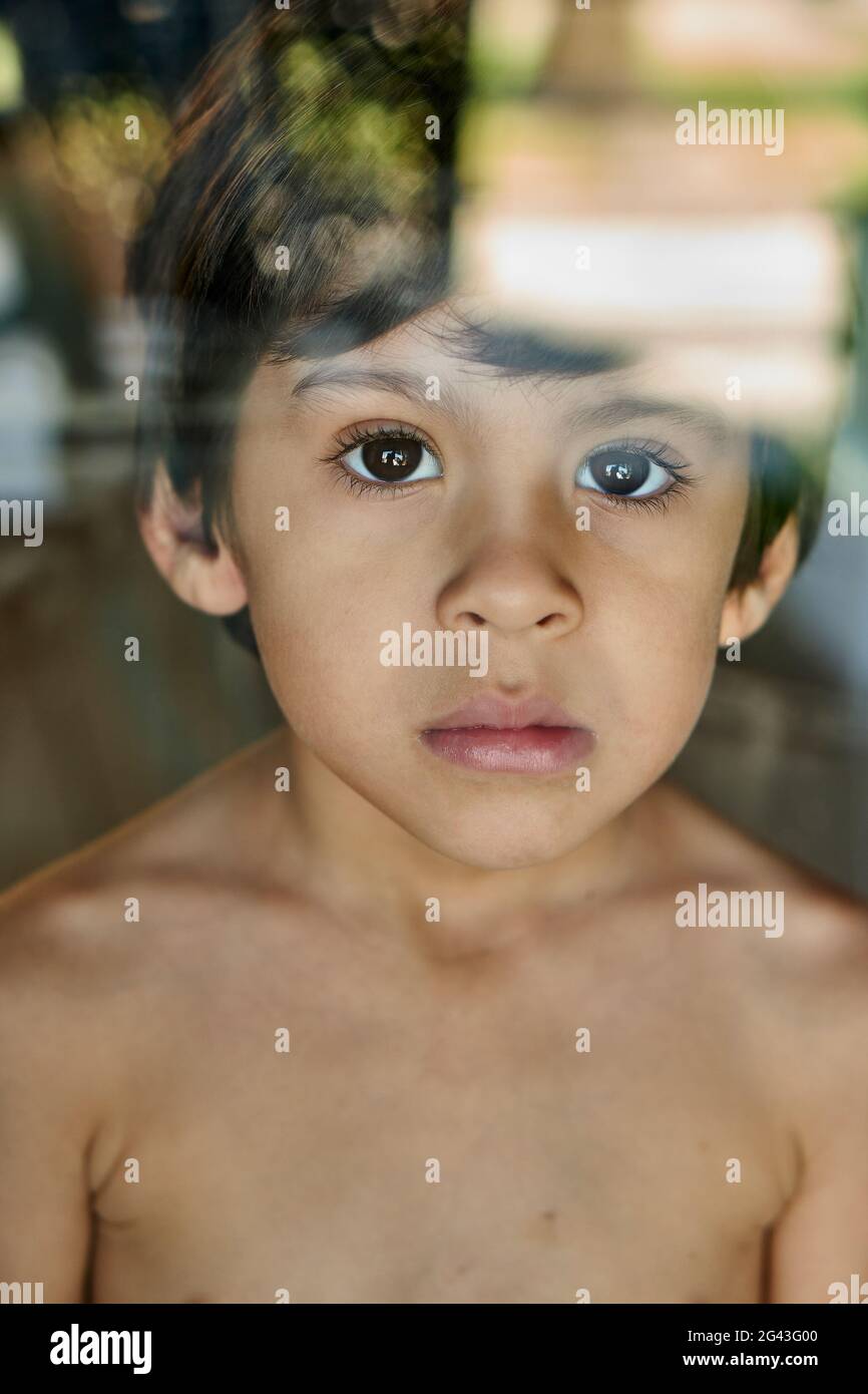 little boy just looking straight ahead from behind glass window, sad Stock Photo