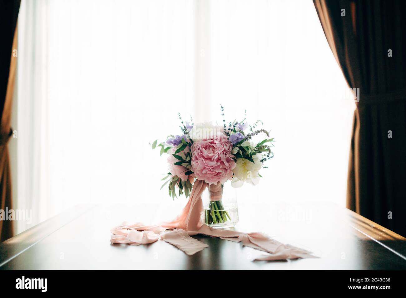 Bridal bouquet of white and pink peonies, olive branches, lavender and campanula with pink ribbons in the glass vase on the tabl Stock Photo
