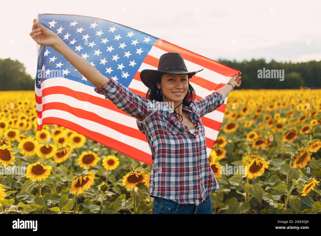 Young smiling woman with American flag in the sunflower field. 4th of July Independence Day USA concept. Stock Photo