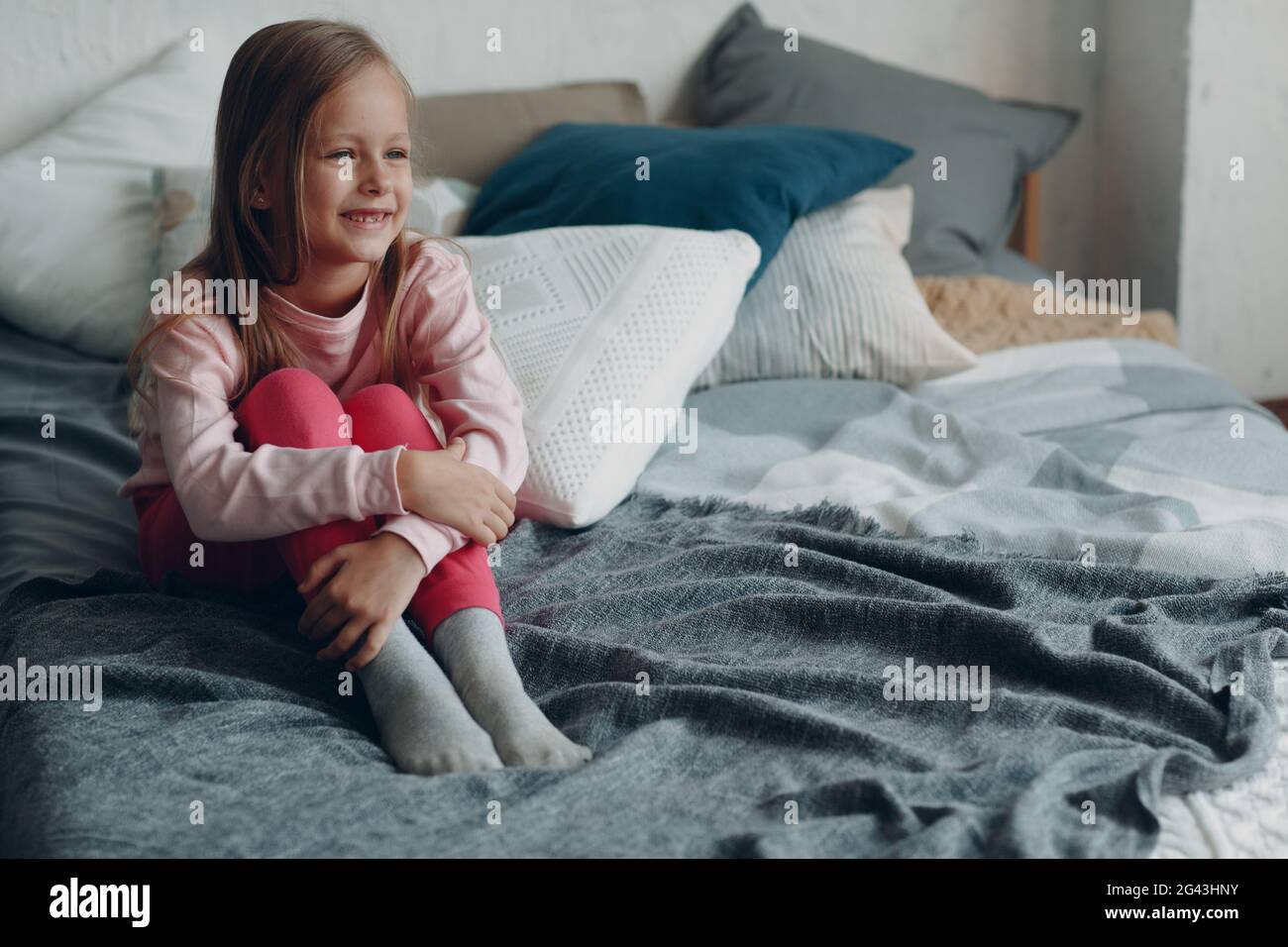 Positive smiling little girl sitting on bed Stock Photo - Alamy