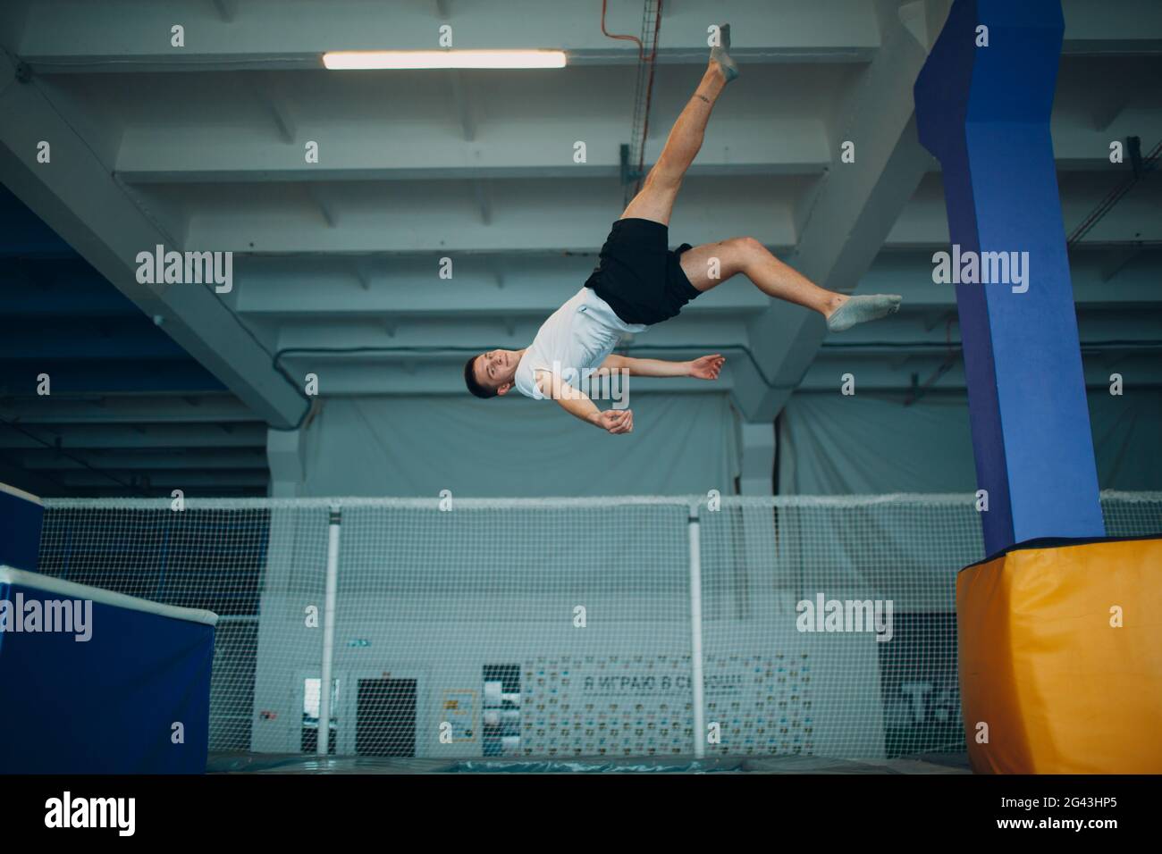 Young man acrobat jumping on trampoline indoor. Stock Photo