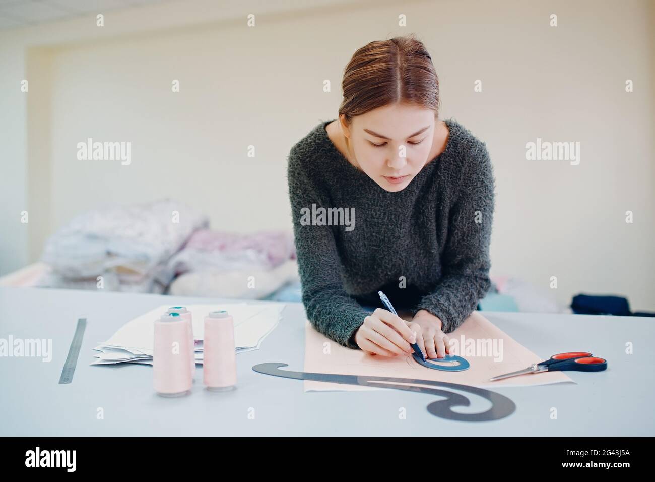 Young beautiful seamstress cutter clothing designer with pattern and template blueprint in garment factory. Stock Photo