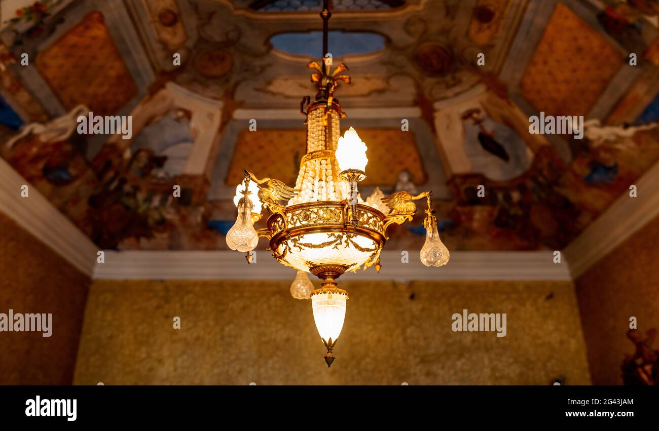 Empire style golden chandelier. Antique chandelier on the ceiling with the lights on. Stock Photo