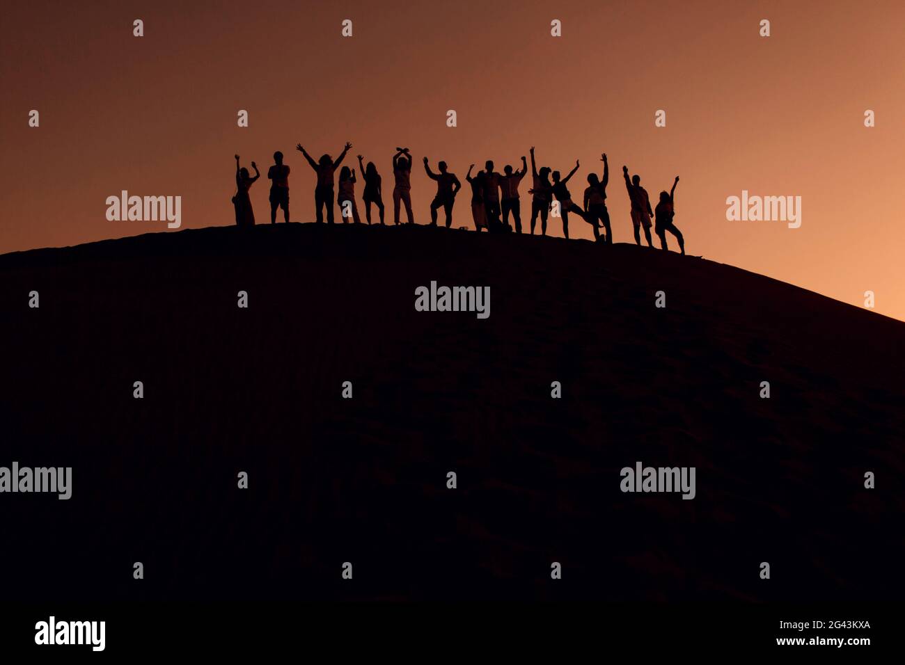 People standing on top of dune in desert with hands up. Silhouettes at ...