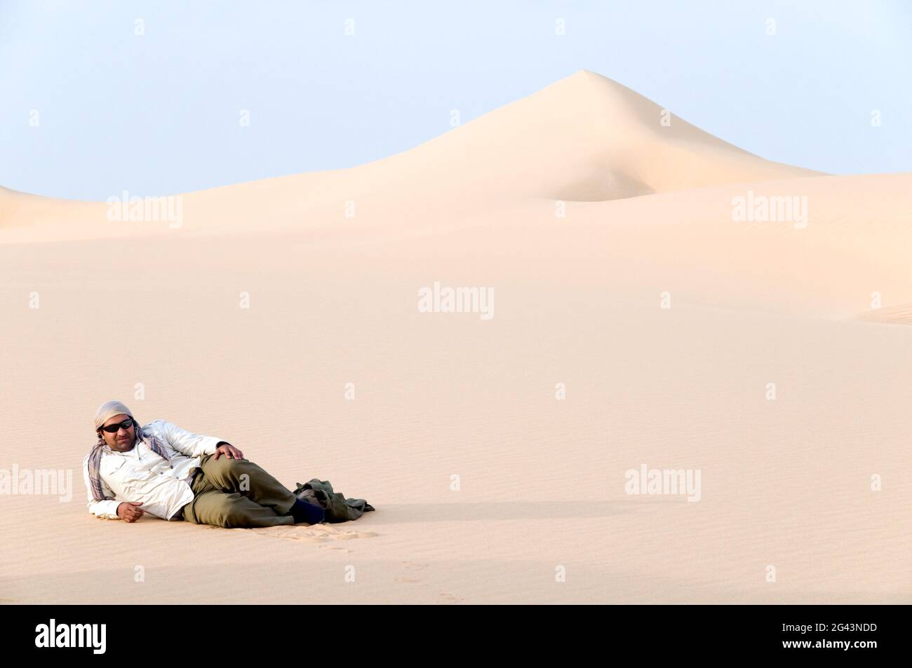An Egyptian Sahara desert guide has a rest on sand dune in the Great Sand Sea region of the Wester Desert in southwest Egypt. Stock Photo