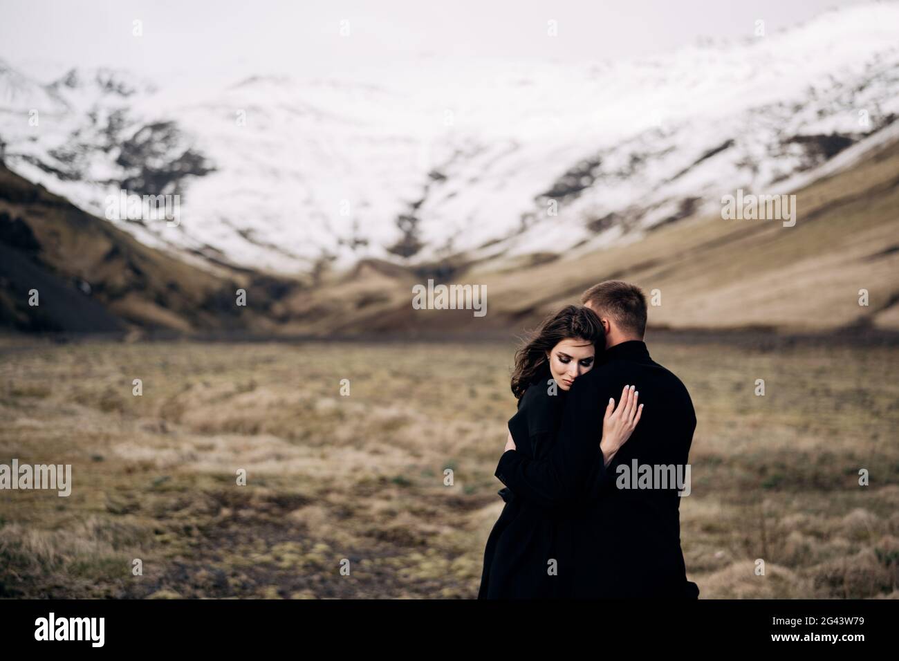 Destination Iceland wedding. Wedding couple on a background of snowy mountains. The bride and groom in black coats are hugging i Stock Photo