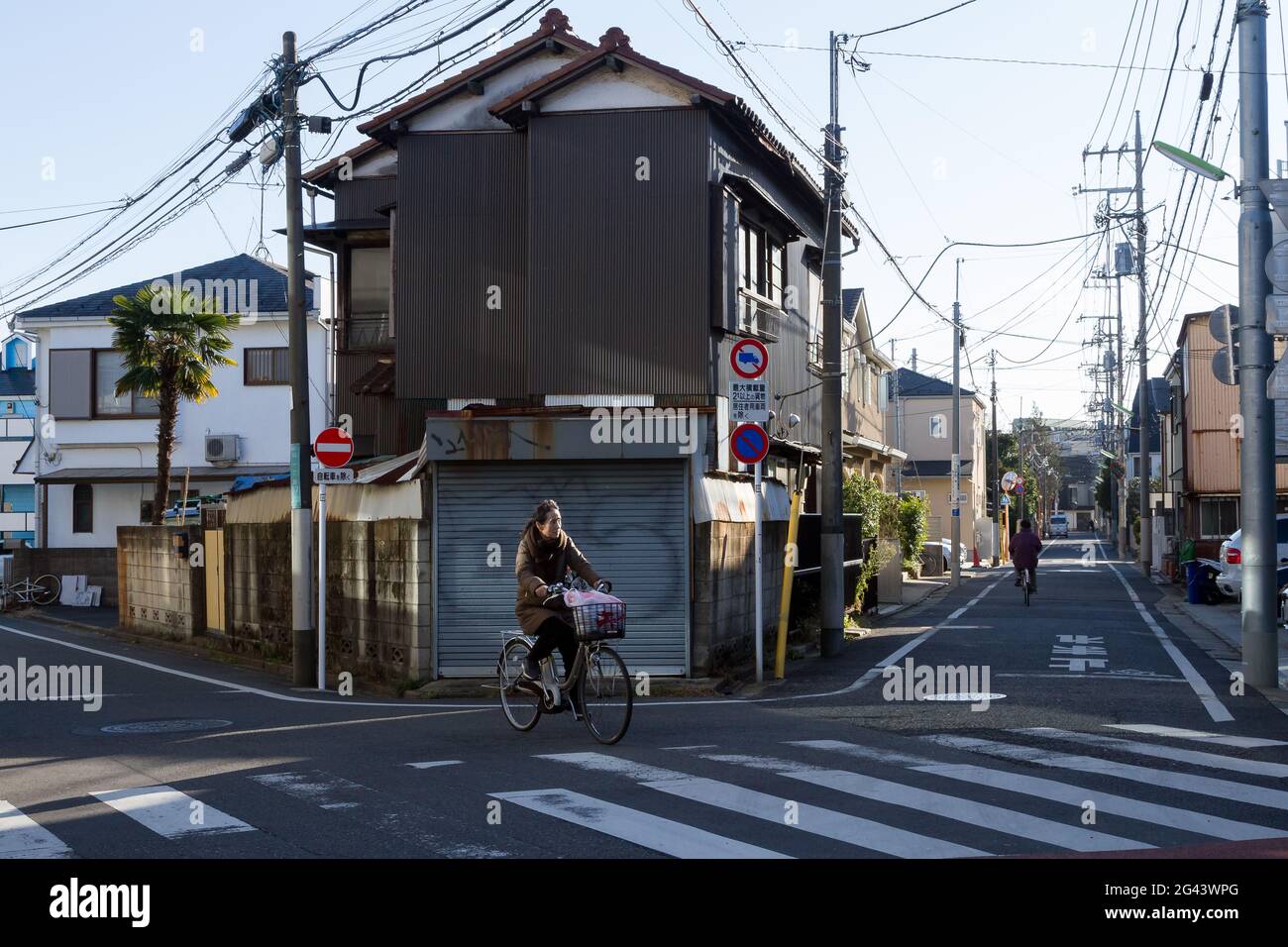 A Japanese woman rides a bicycle at a crossing in Suburban Setagaya Ward,, Gotokuji, Tokyo, Japan. Stock Photo