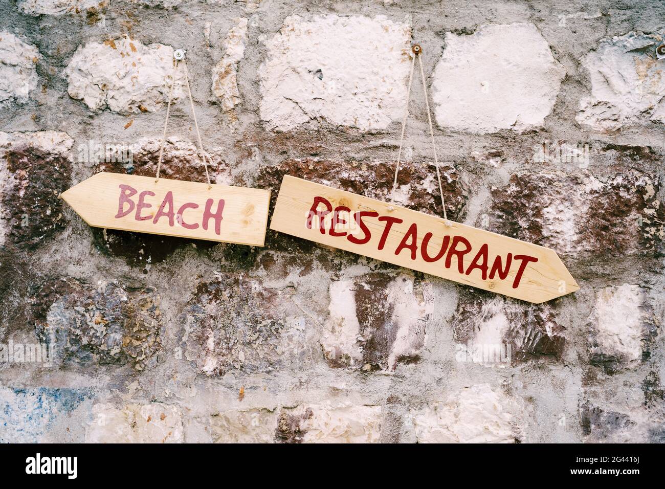 Two multidirectional signs with inscriptions hang on a stone wall Stock Photo