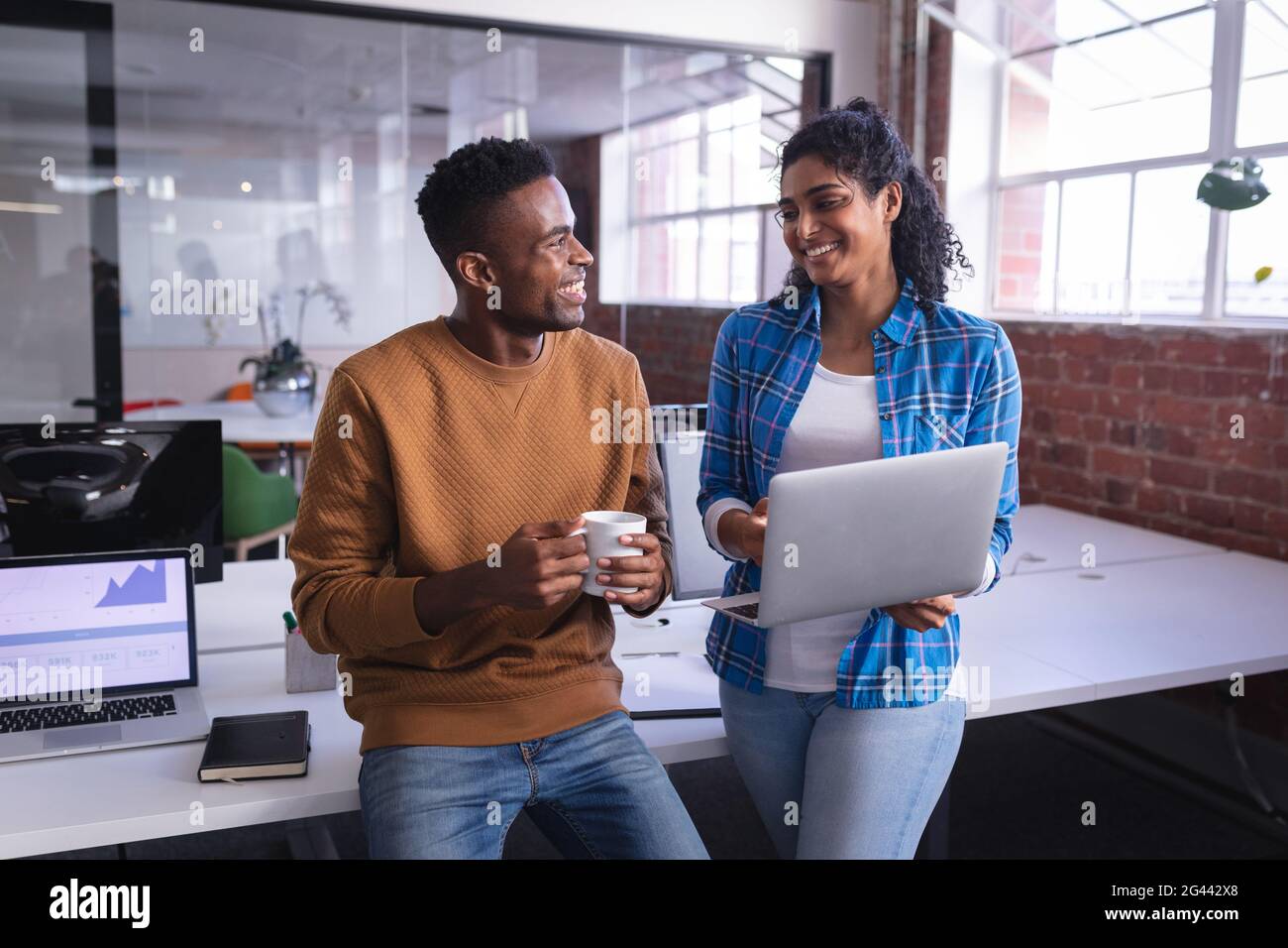 Happy diverse male and female colleagues at work standing discussing in ...