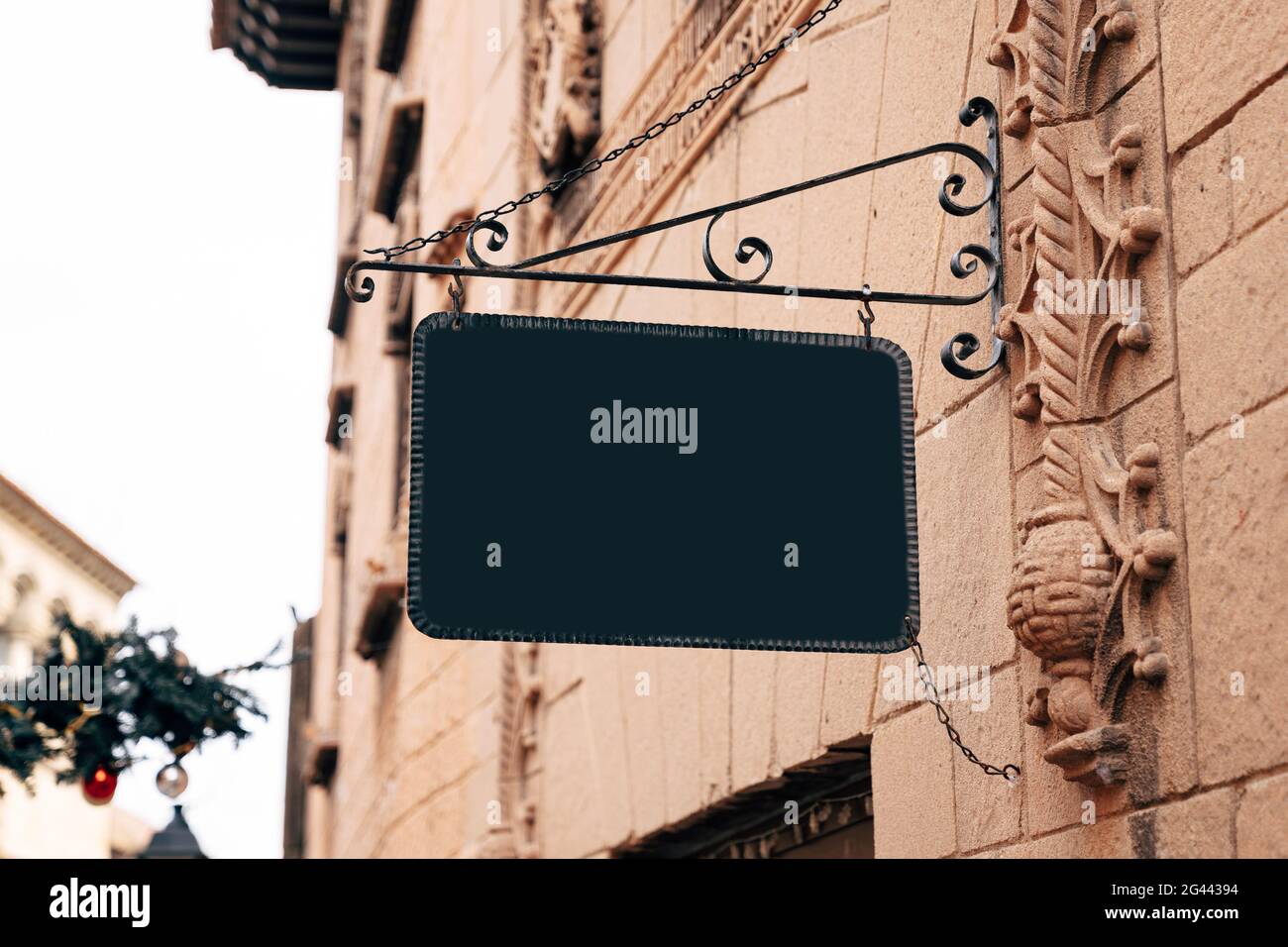 Stylish rectangular blank sign in a wrought-iron frame hangs on the stone wall of an ancient building Stock Photo