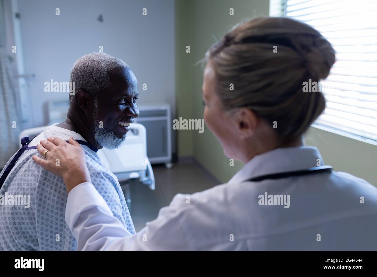 Diverse female doctor and male patient sitting on hospital bed smiling ...