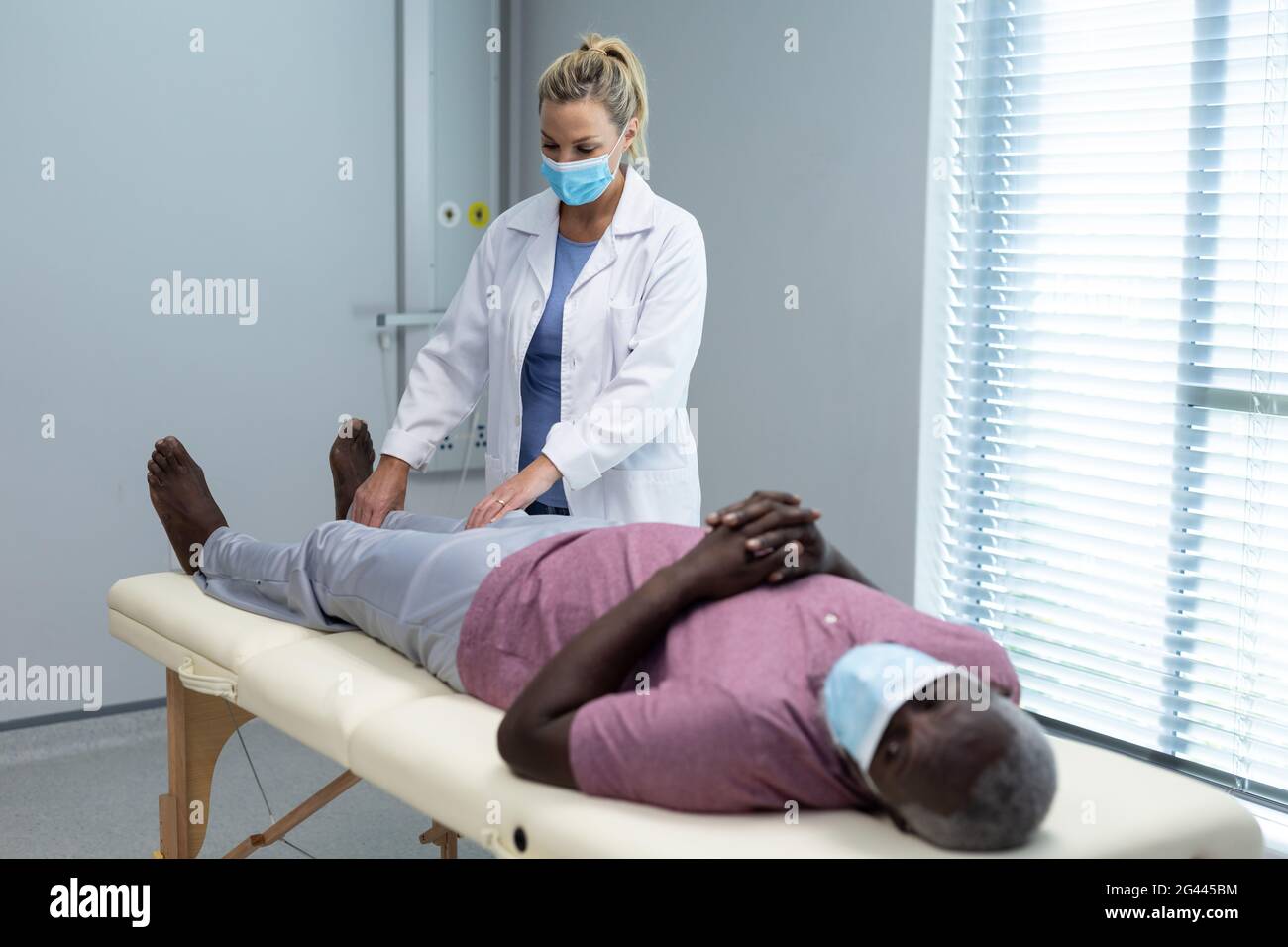 Caucasian female physiotherapist wearing mask stretching leg of african american male patient Stock Photo