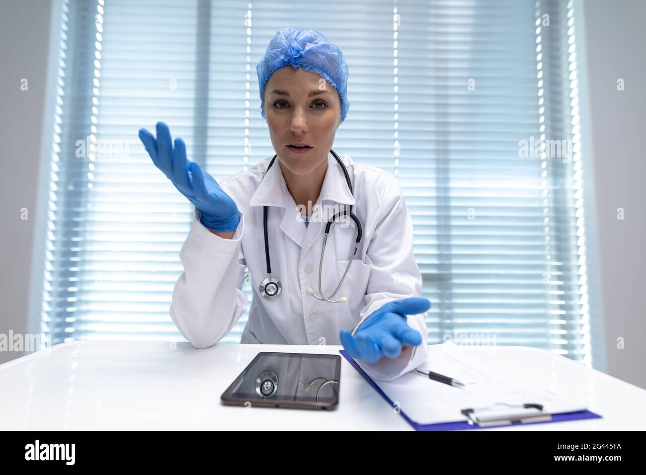 Caucasian female doctor at desk talking and gesturing during video call ...