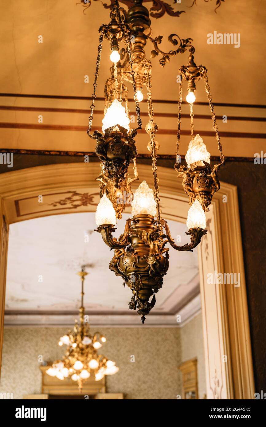 Copper chandelier on the ceiling. Antique lamps on chains. Glass shades and floral designs. Stock Photo