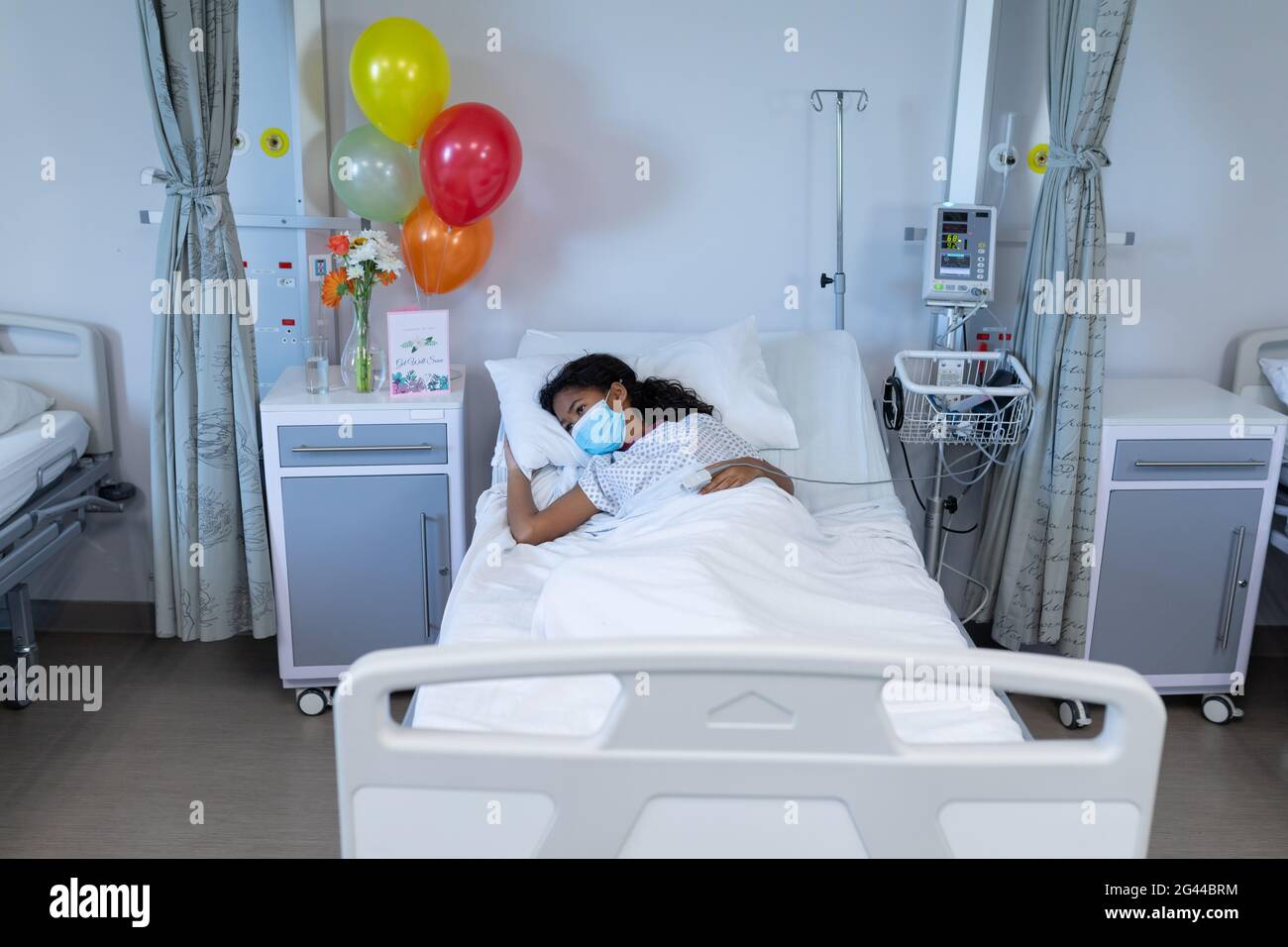 Mixed race sick girl lying in hospital bed wearing face mask and fingertip pulse oximeter Stock Photo