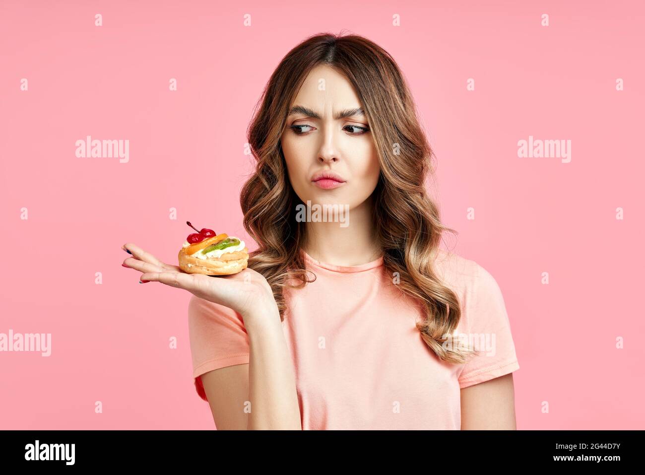 Dieting concept. Unhappy pretty woman looking to pastry cake Stock Photo