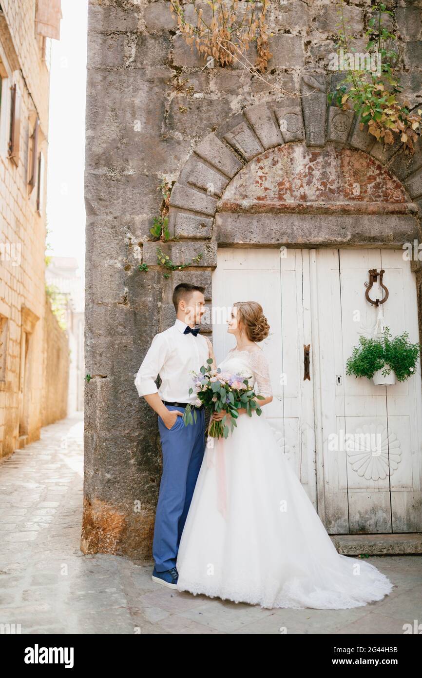 The bride and groom stand hugging near an old white wooden door in the ...