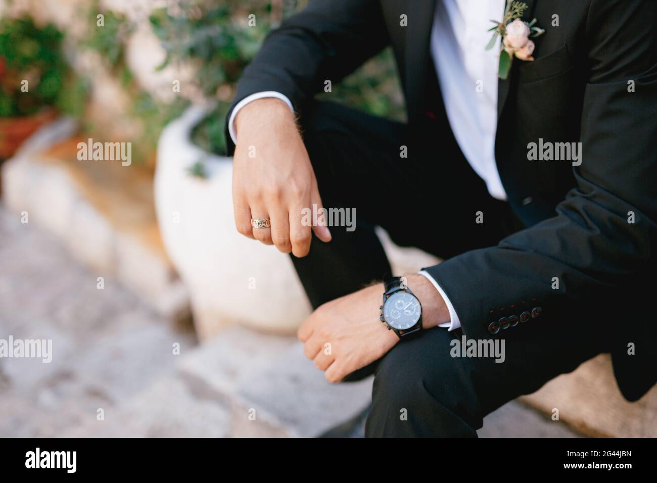 A man in a suit with a boutonniere and a wristwatch is sitting on a step, close-up Stock Photo