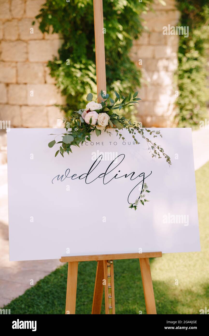 White wooden easel with an inscription on the background of a stone wall and greenery. Caption: Welcome to our wedding Stock Photo