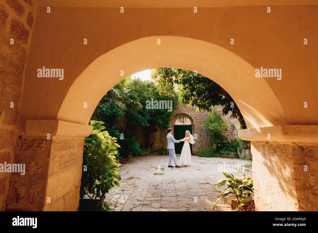 The bride and groom dancing and circling in the coutryard in the old town of Perast, view through the arch Stock Photo