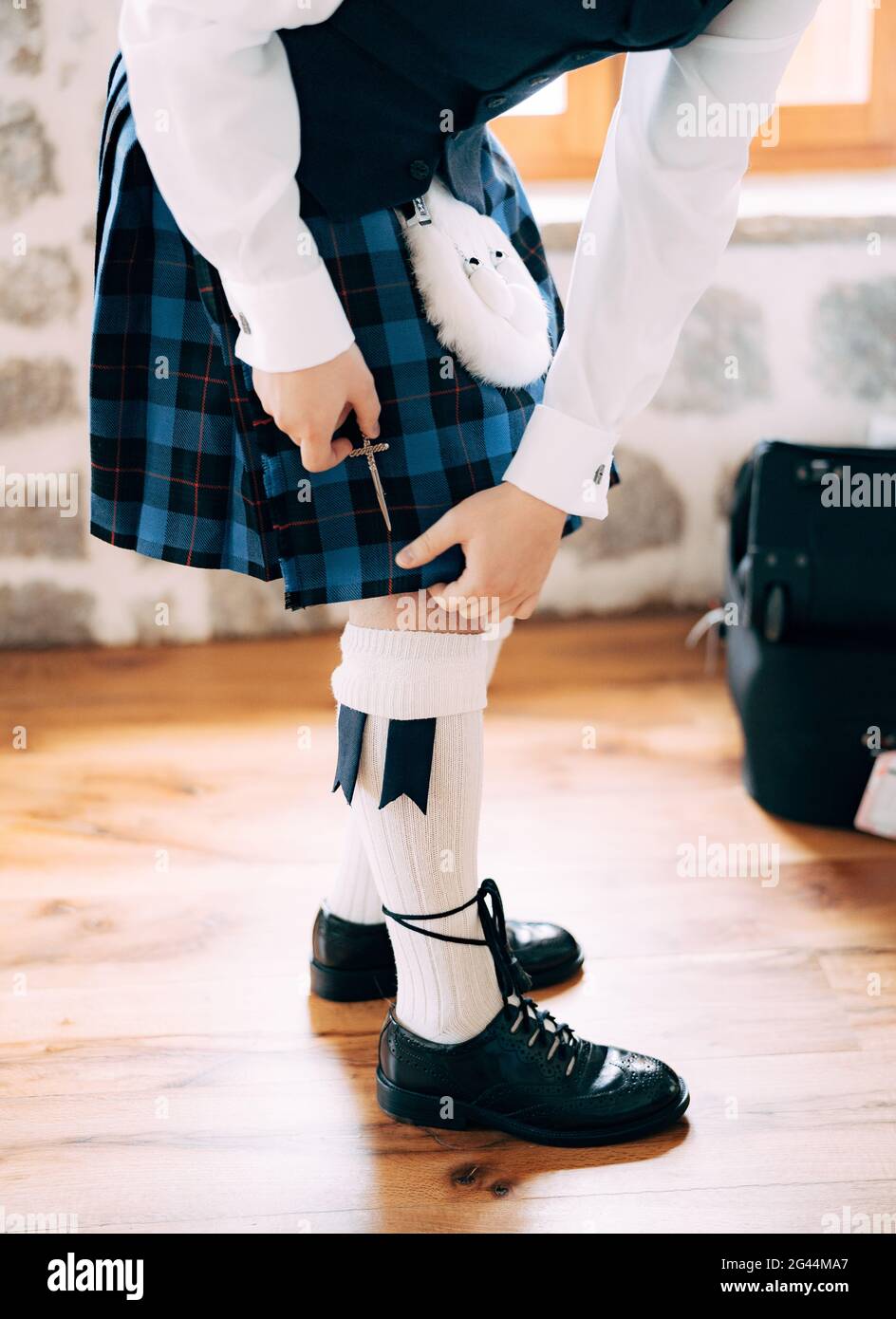 Preparing for a Scottish wedding. Man in high socks, sporran and shoes with long laces attaches a small sword to the kilt Stock Photo