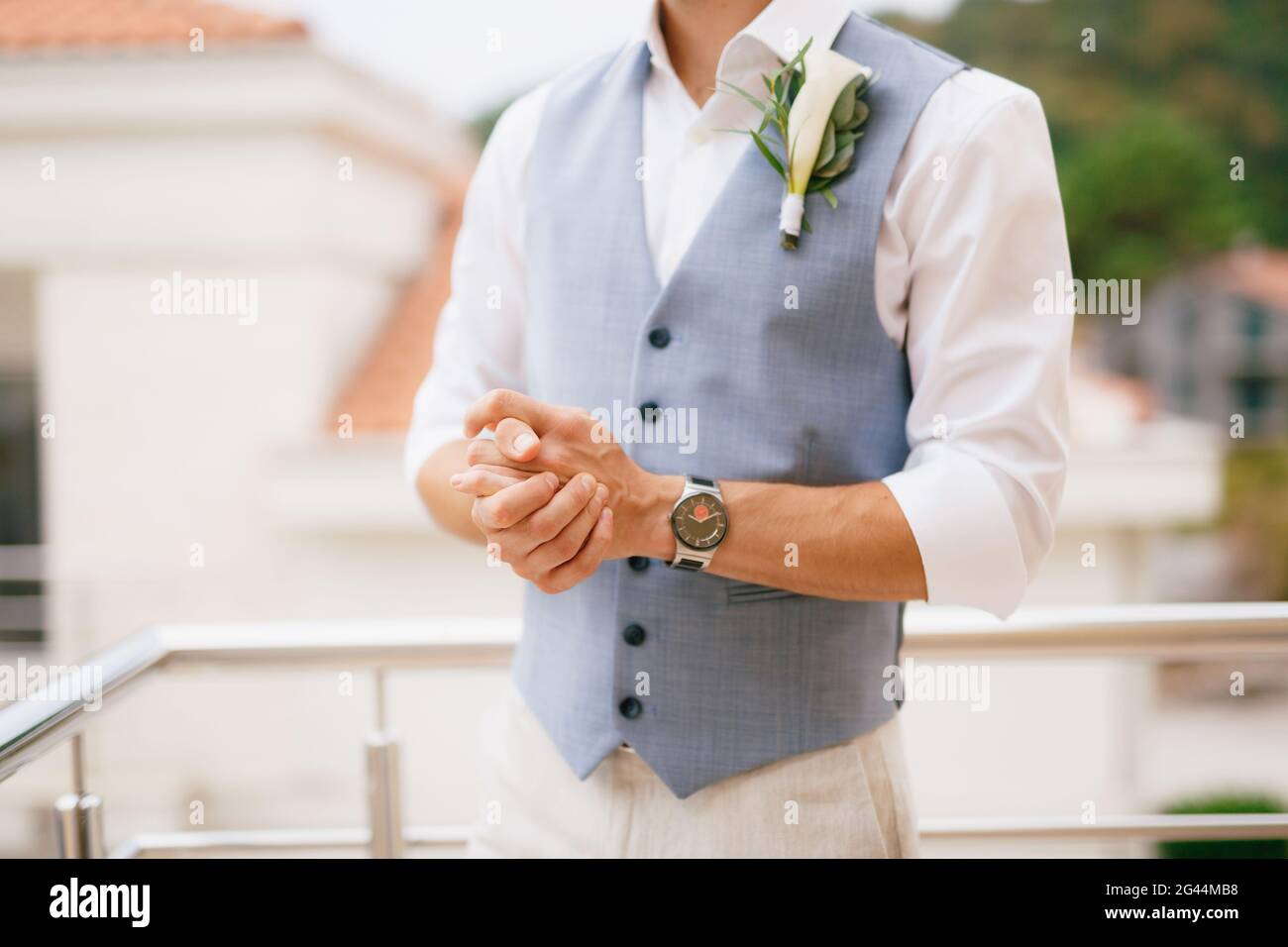 The groom in a shirt and vest with a boutonniere stands on the balcony in the morning before the wedding ceremony Stock Photo