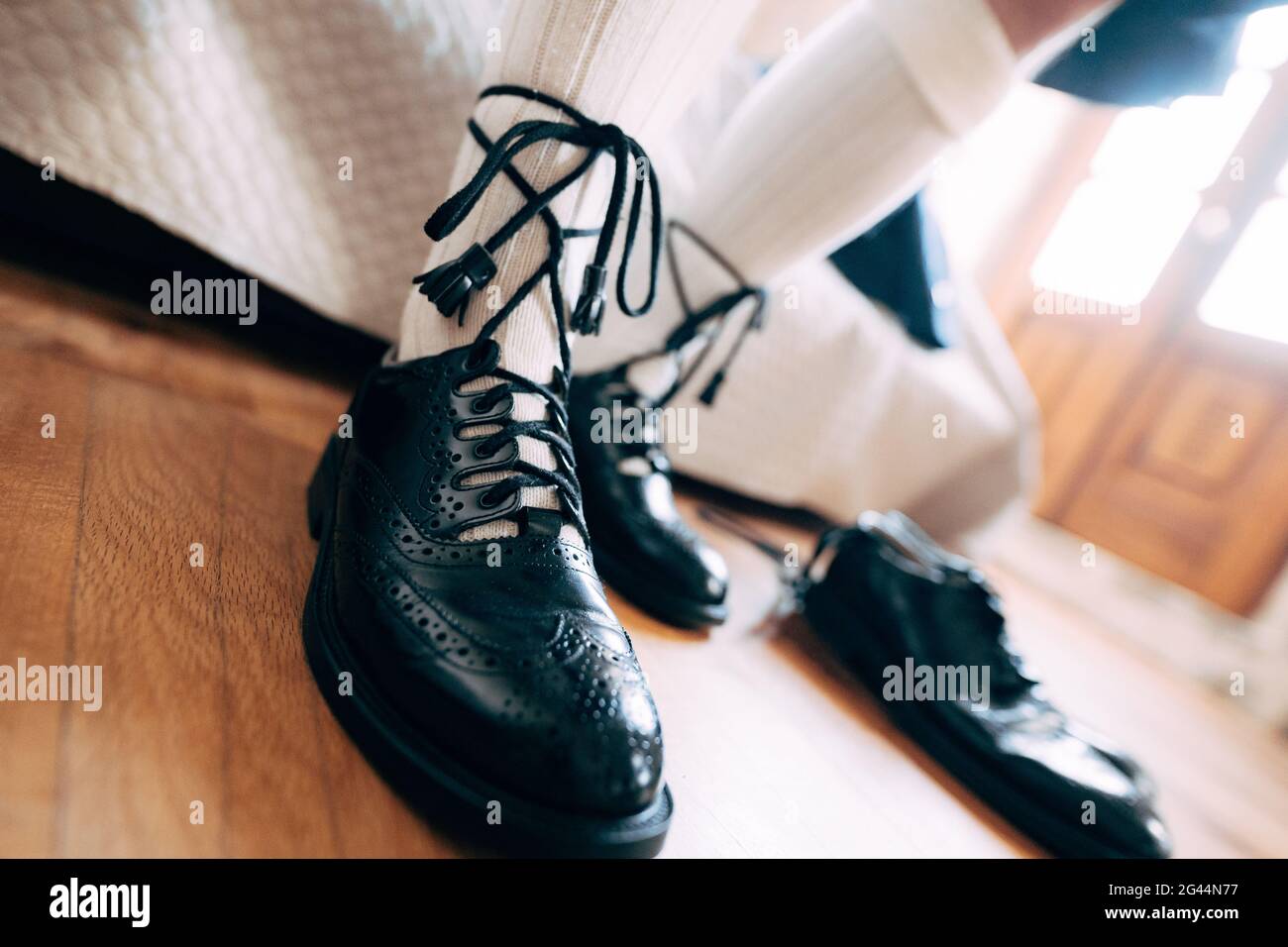 Preparing for a Scottish wedding. Man in a kilt, high socks and shoes laced with long laces. Nearby a pair of black shoes Stock Photo