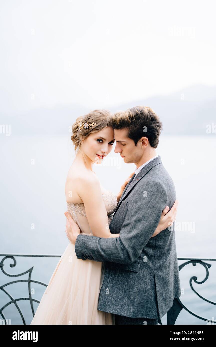 Newlyweds hug near a wrought-iron fence against the backdrop of Lake Como. Close up Stock Photo