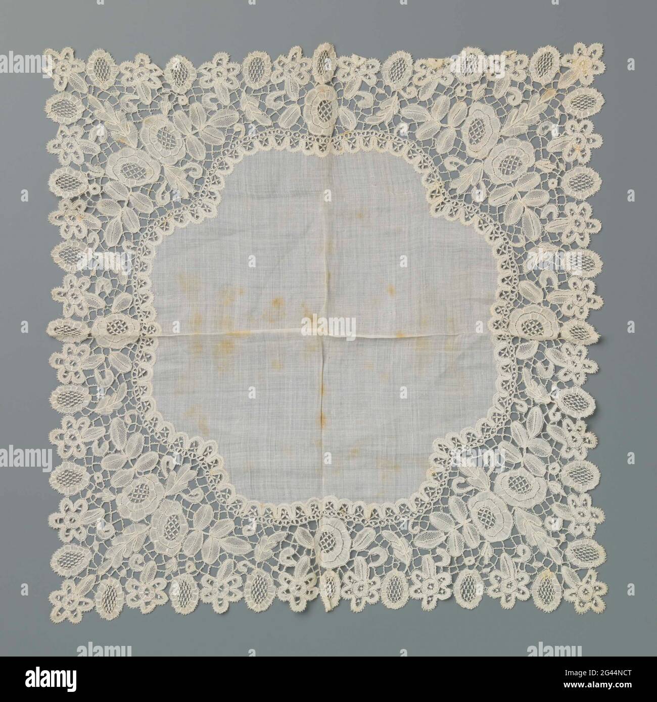 Handkerchief of white batist with an edge of Honitonker. Natural batist handkerchief with an edge natural colosside: Honiton side. The batist interior has four lobes. The symmetrical pattern on the side exists in the corners of two diagonally placed roses between leaves. The sloping edge exists alternately from a five-spinning flour and an oval with fill pattern. Above every middle oval (halfway each side) is a comparable oval flower, with an α-symmetrical additional petals edge. The inner edge, where the side is sewn to the batist, consists of a decorative edge of connected ovals on which Hal Stock Photo