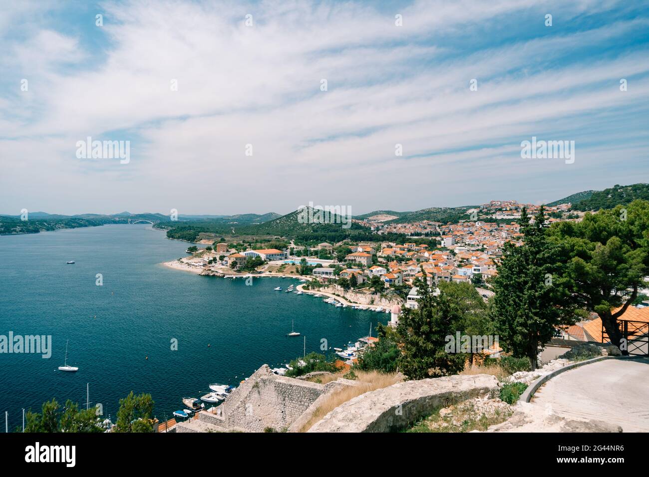 View of the sea and the pier with white yachts from behind the roofs of old houses in Sibenik. Side view Stock Photo