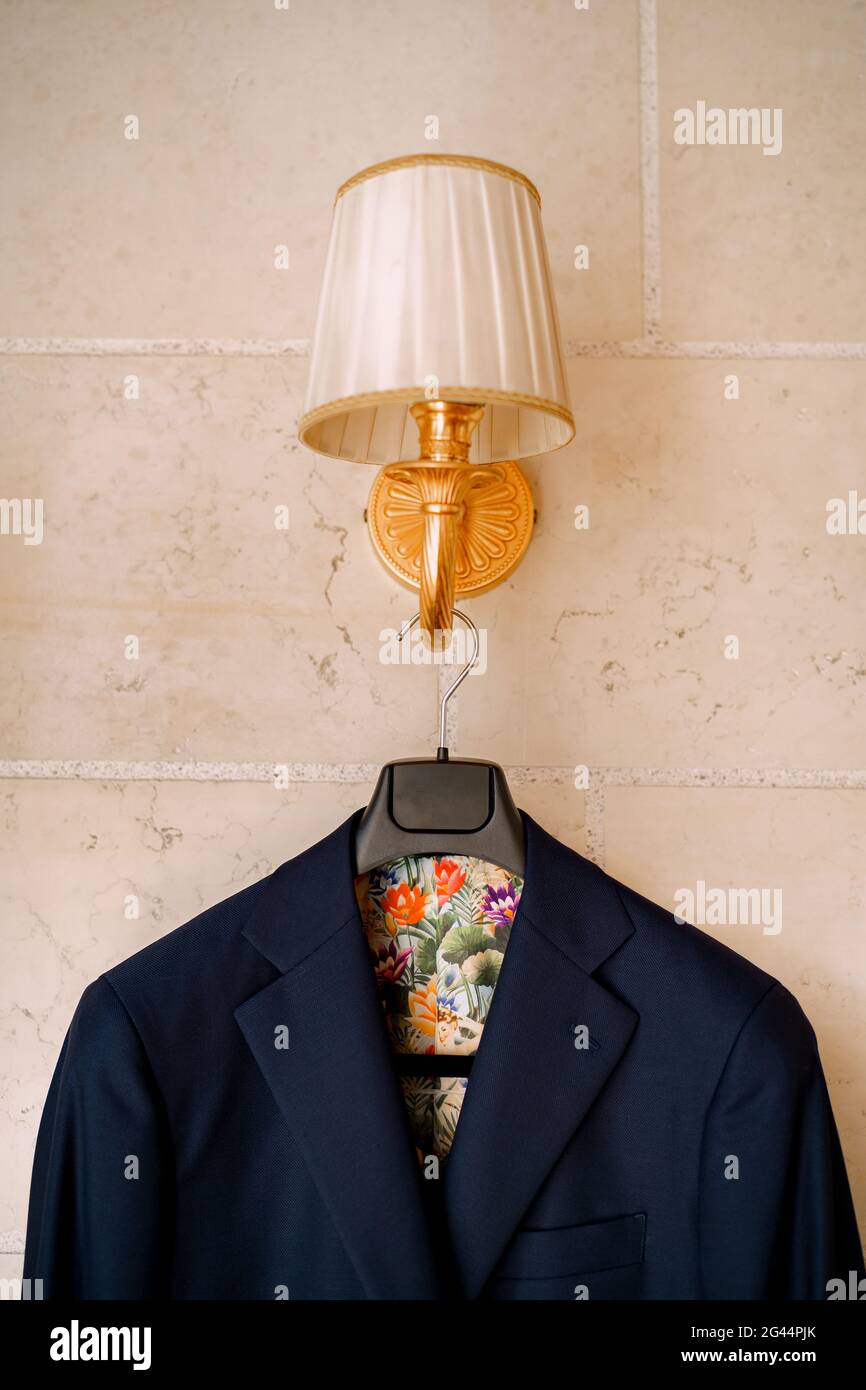 A blue jacket with a colorful lining hangs from a wall lamp on a black hanger. Stock Photo