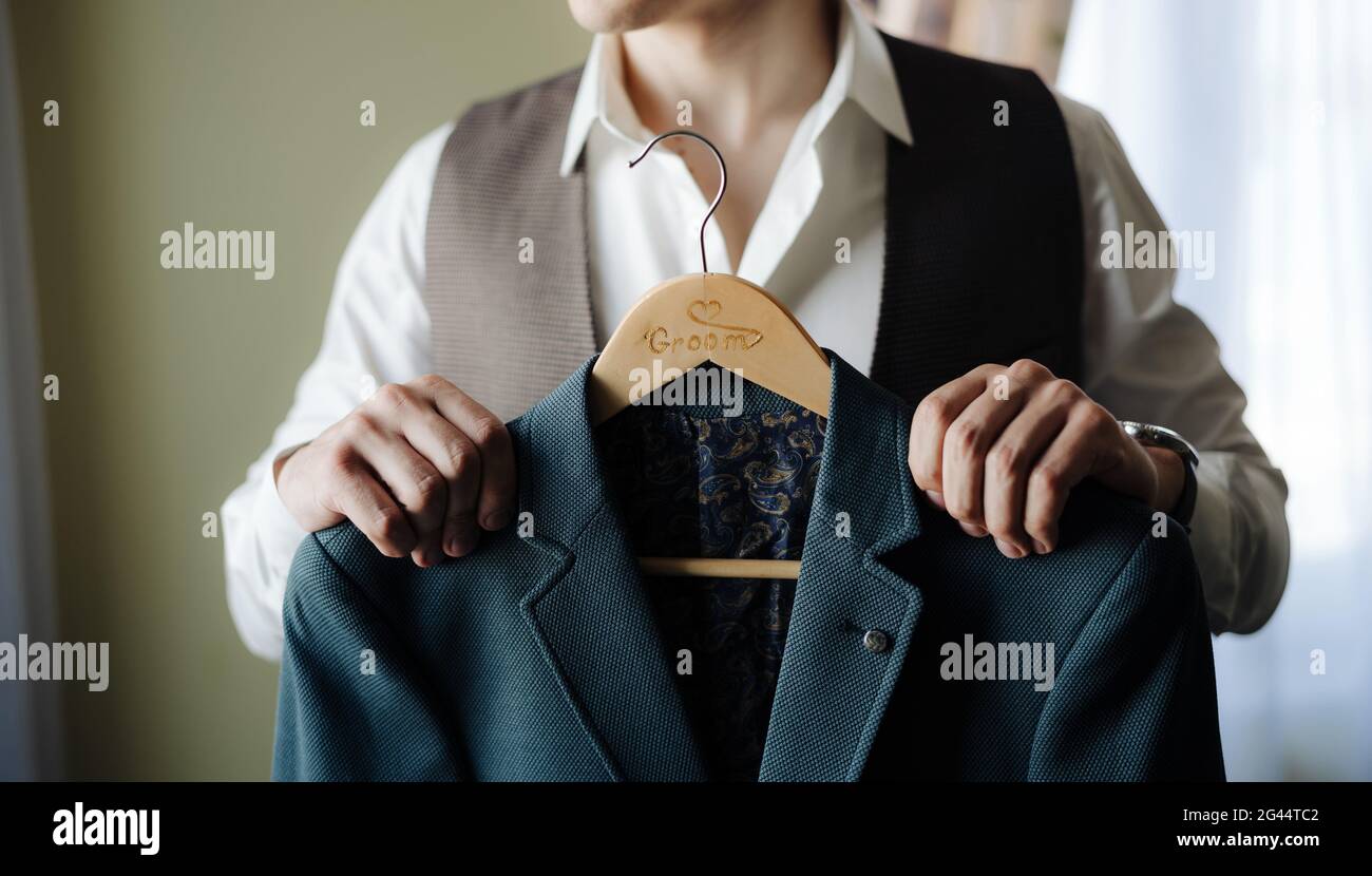 Groom in a white shirt and vest holds a jacket on a hanger Stock Photo