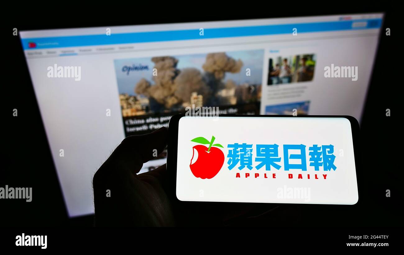 Person holding smartphone with logo of Hong Kong newspaper Apple Daily on screen in front of website. Focus on phone display. Stock Photo