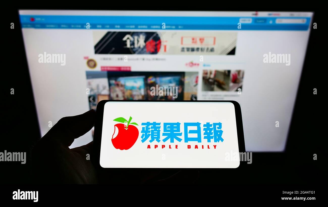 Person holding mobile phone with logo of Hong Kong newspaper Apple Daily on screen in front of business web page. Focus on phone display. Stock Photo