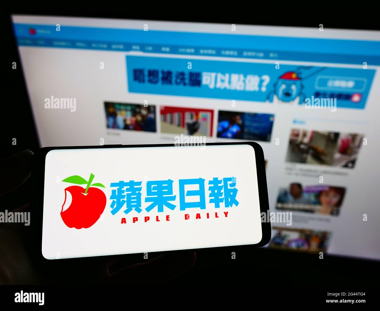 Person holding cellphone with logo of Hong Kong newspaper Apple Daily on screen in front of company website. Focus on phone display. Stock Photo