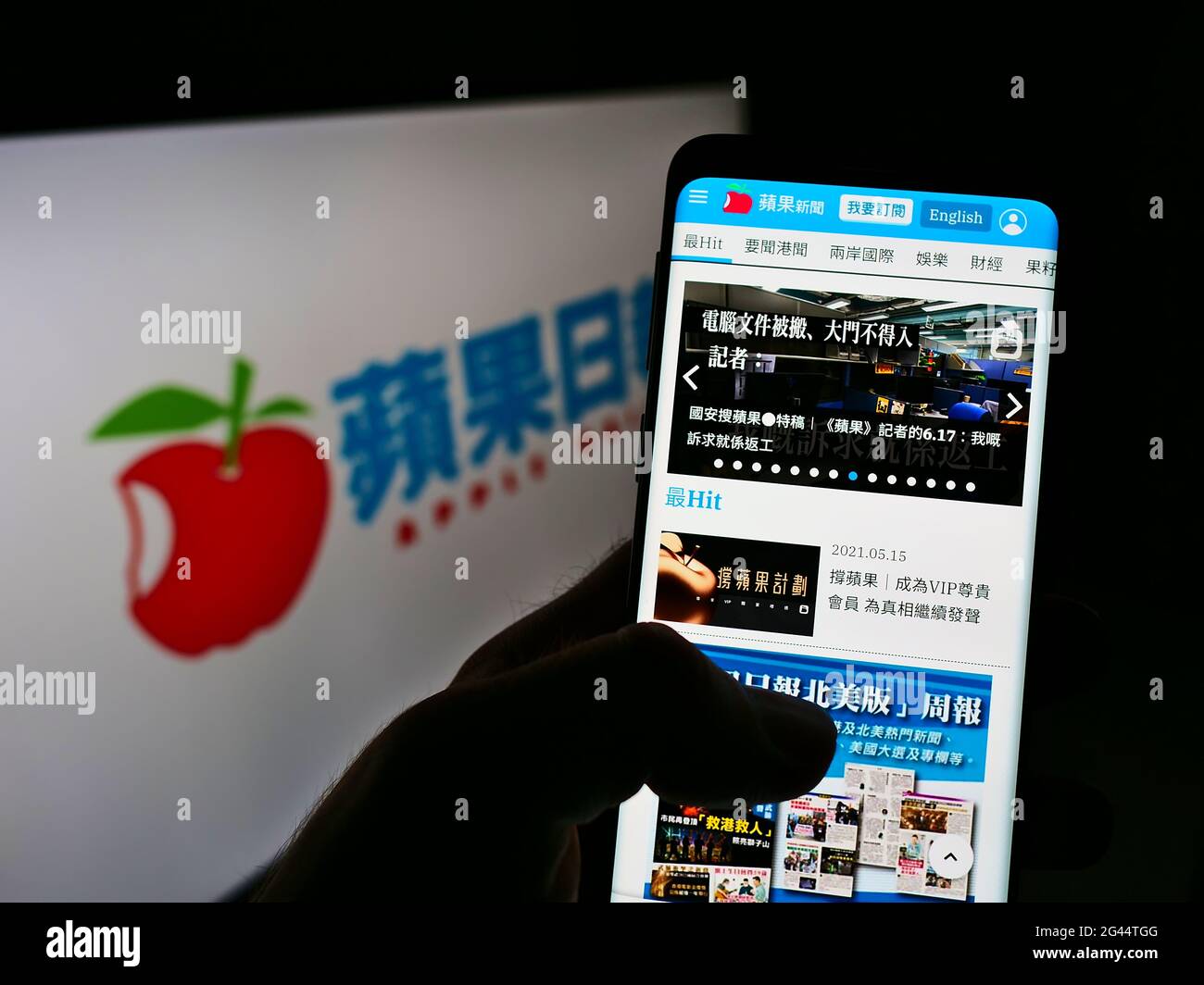 Person holding cellphone with webpage of Hong Kong newspaper Apple Daily on screen in front of business logo. Focus on center of phone display. Stock Photo