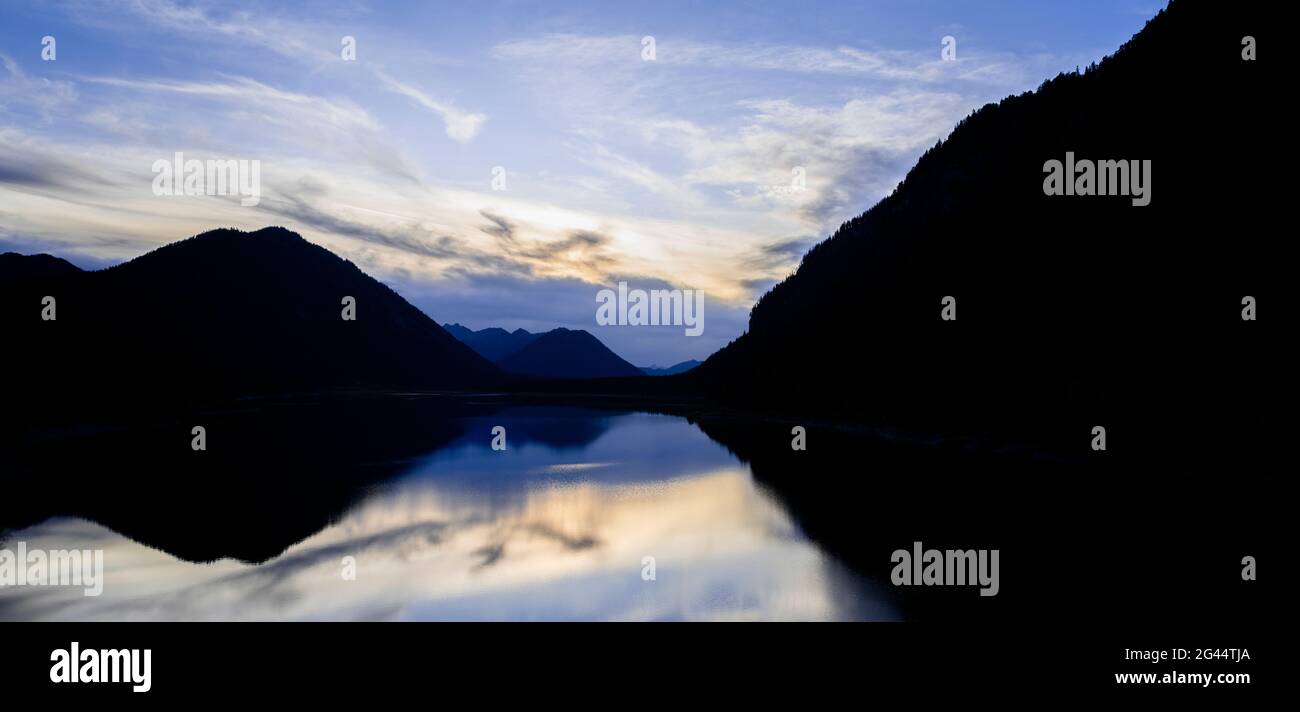 Silhouetted mountains reflecting in Sylvenstein Lake at sunset, Bavaria, Germany Stock Photo