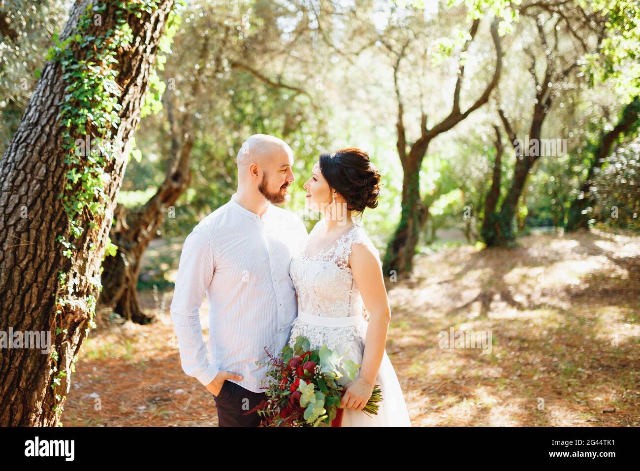 The bride and groom with a bouquet stand hugging among the trees in an ...