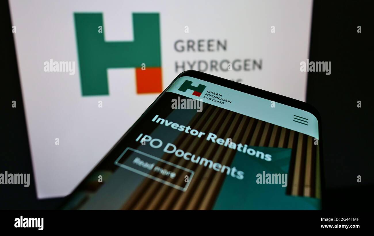 Person holding cellphone with webpage of Danish energy company Green Hydrogen Systems AS on screen with logo. Focus on center of phone display. Stock Photo