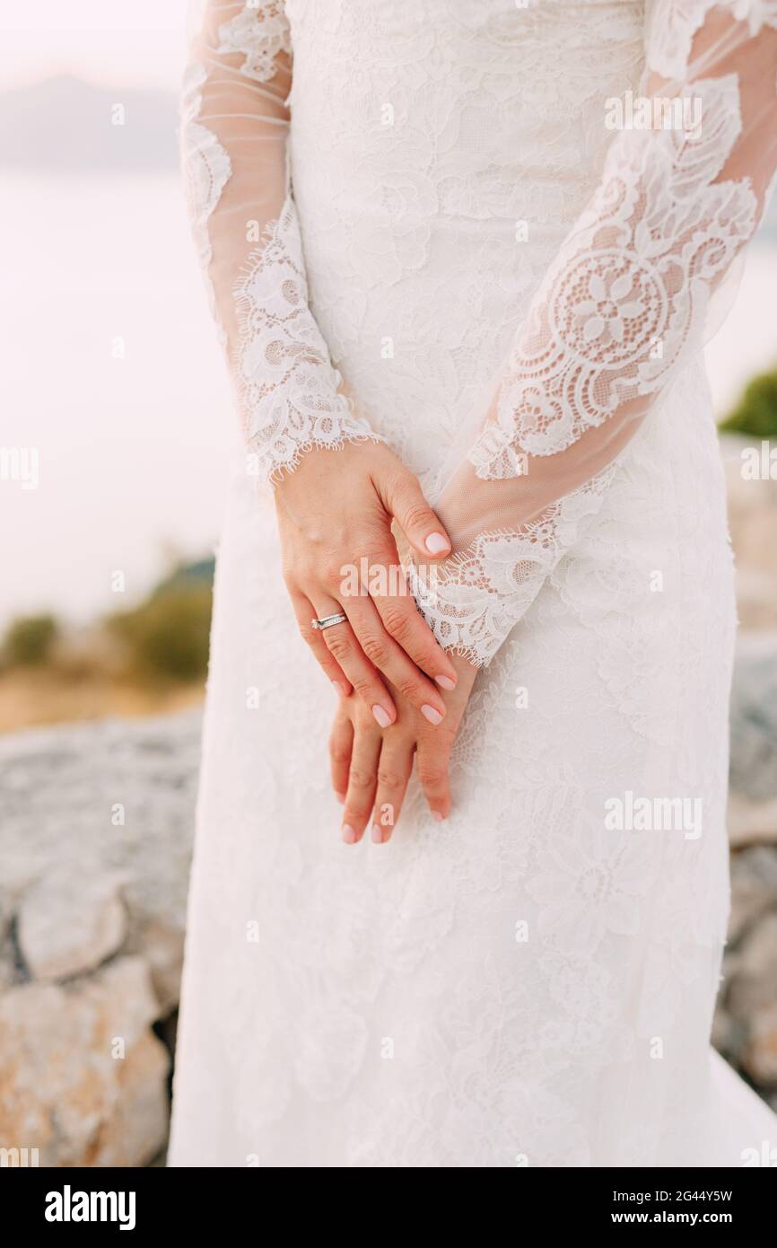 The bride in dress with lace sleeves folded her hands with a wedding ring on her finger, close-up Stock Photo