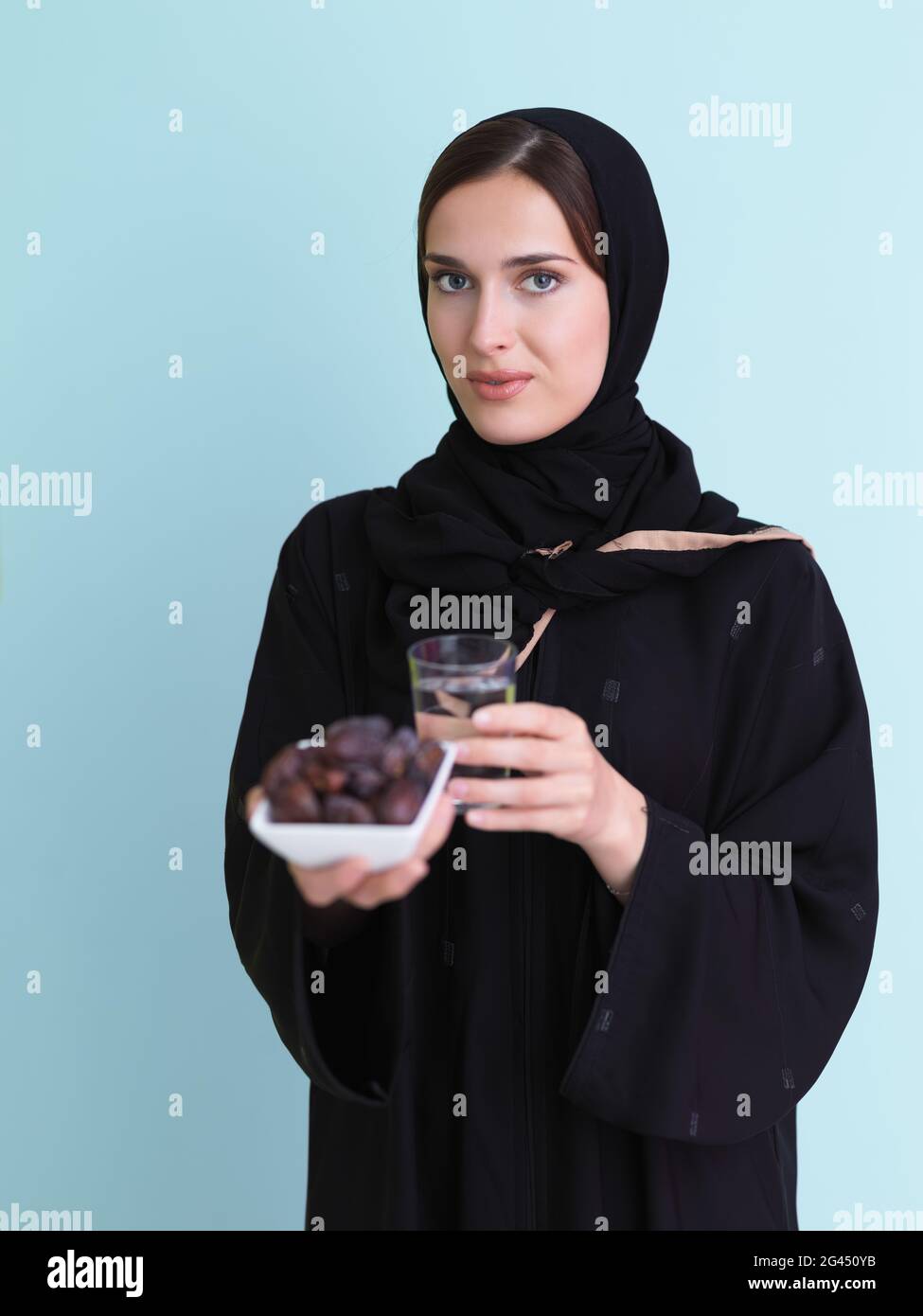 Modern muslim woman in abaya holding a date fruit and glass of water in front of her Stock Photo