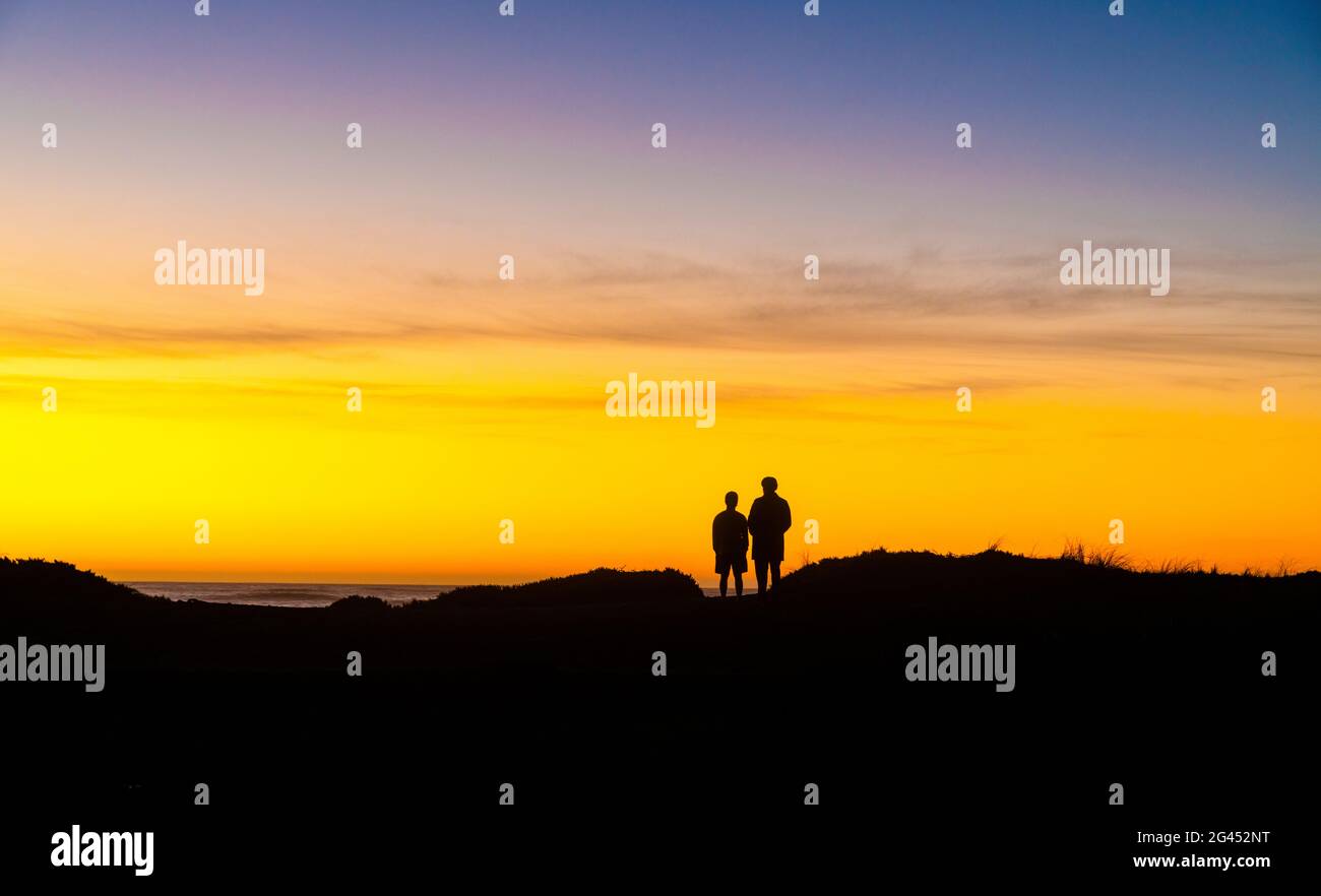 Silhouetted people watching sunset over Pacific Ocean Stock Photo