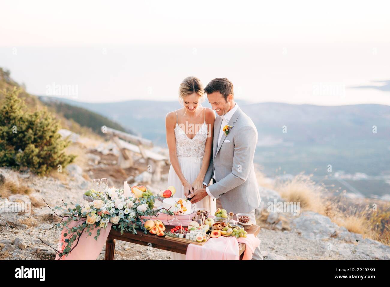 The bride and groom are cutting a cake during a buffet table after the wedding ceremony on Mount Lovcen and smiling Stock Photo