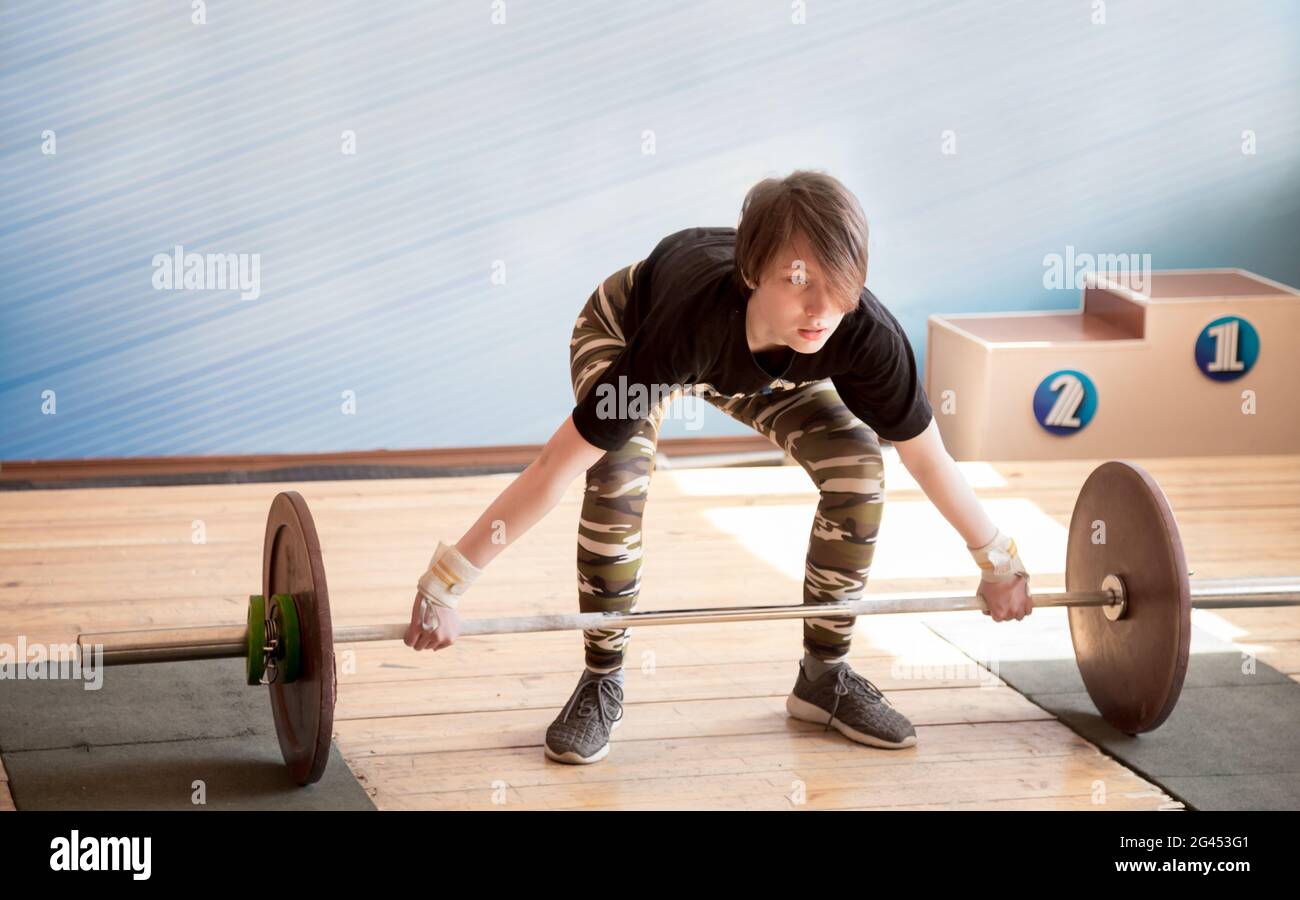 Young caucasian girl of 13 years old does snatch exercise during weightlifting competition with heavy barbell. Kid's weightlifti Stock Photo