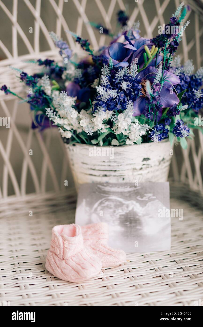 Baby booties on a wicker chair and a bouquet of lavender on a ba Stock Photo