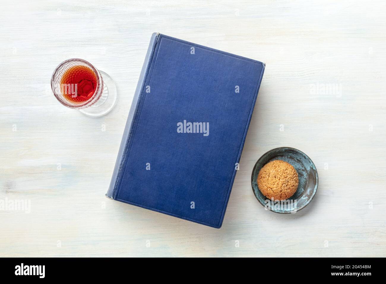 An old book with a glass of dessert wine and a biscuit, shot from above Stock Photo